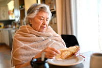 Photo of a grandmother at a kitchen table enjoying a piece of toast