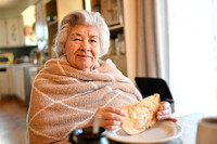 Photo of a grandmother at a kitchen table enjoying a piece of toast