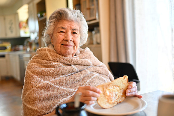 Photo of a grandmother at a kitchen table enjoying a piece of toast